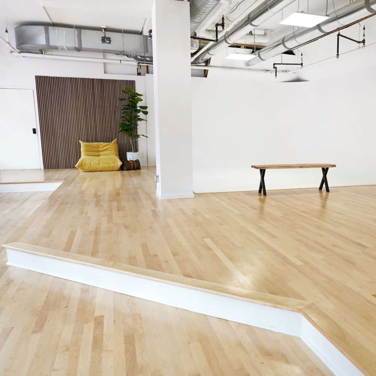 An empty room features wooden flooring, a large sofa, a coffee table, and a small plant against a wall.