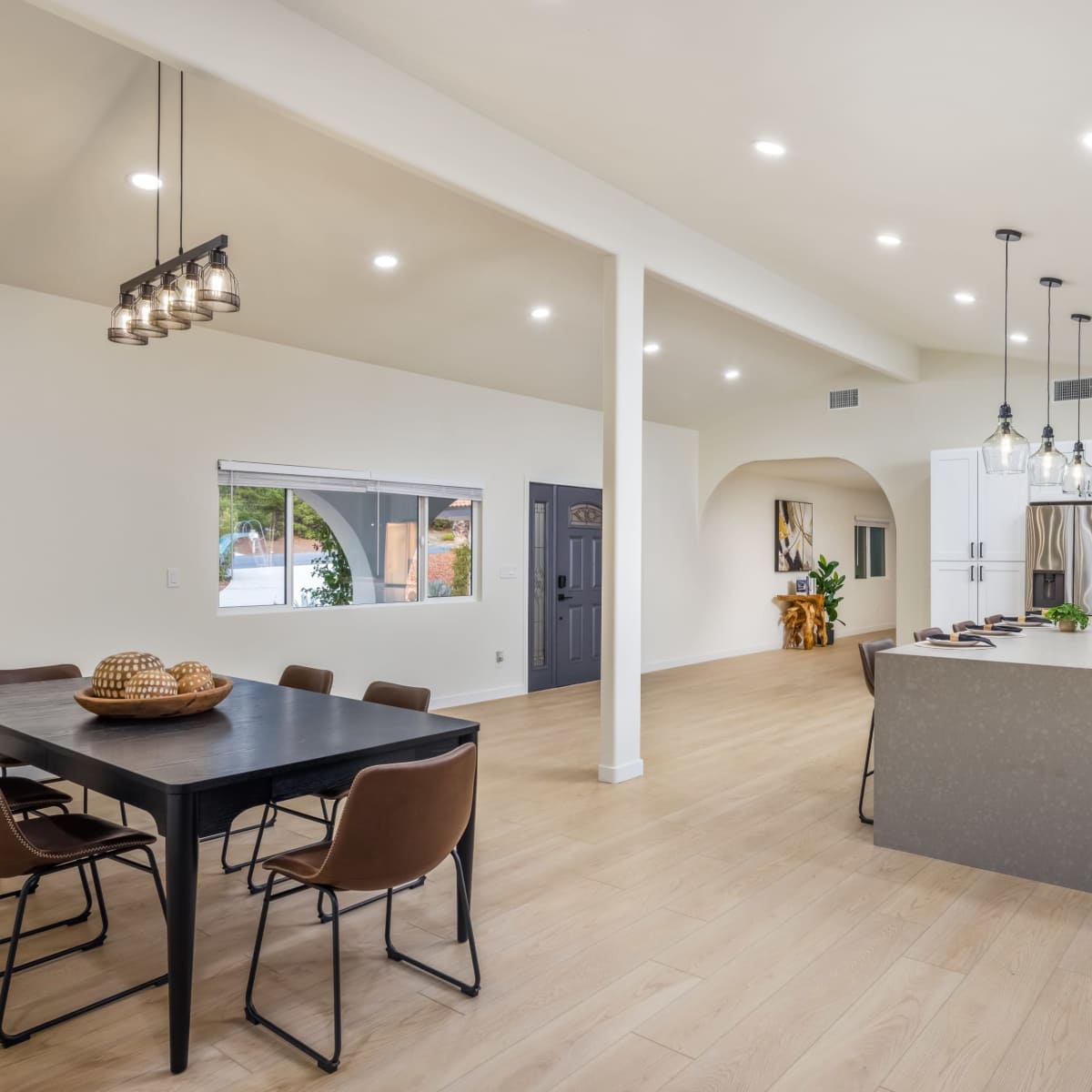 A modern kitchen and dining area with a large island, a dining table with chairs, and bright overhead lighting.