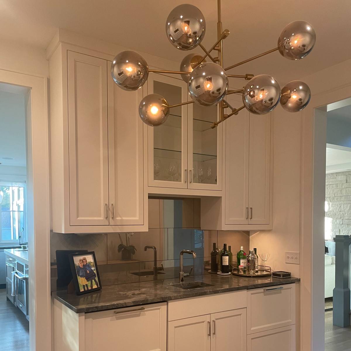 A modern kitchen with white cabinetry, a dark countertop, and a decorative light fixture with spherical bulbs.