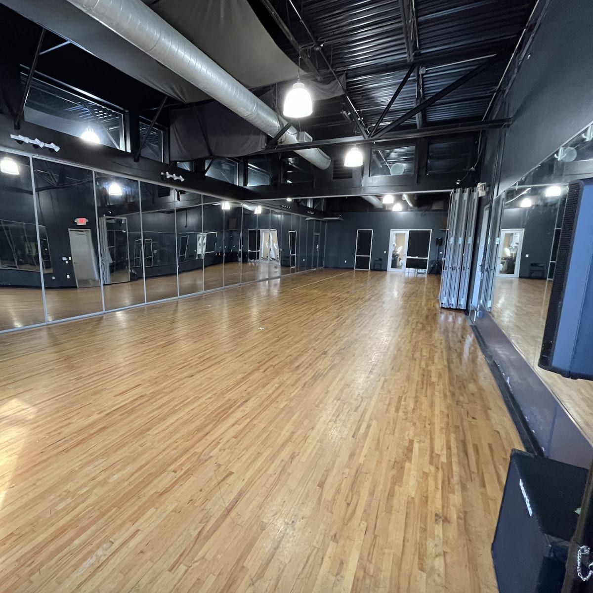 A spacious dance studio featuring a polished wooden floor and large mirrors lining one wall.