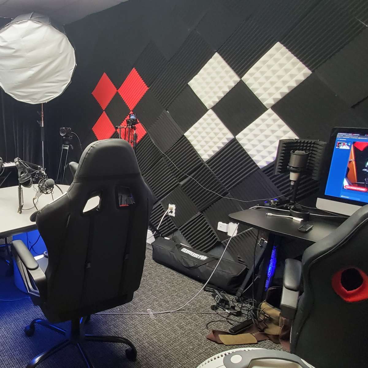 A soundproof recording studio features a table with several chairs, illuminated by a soft light source, and walls decorated with black and red acoustic panels.