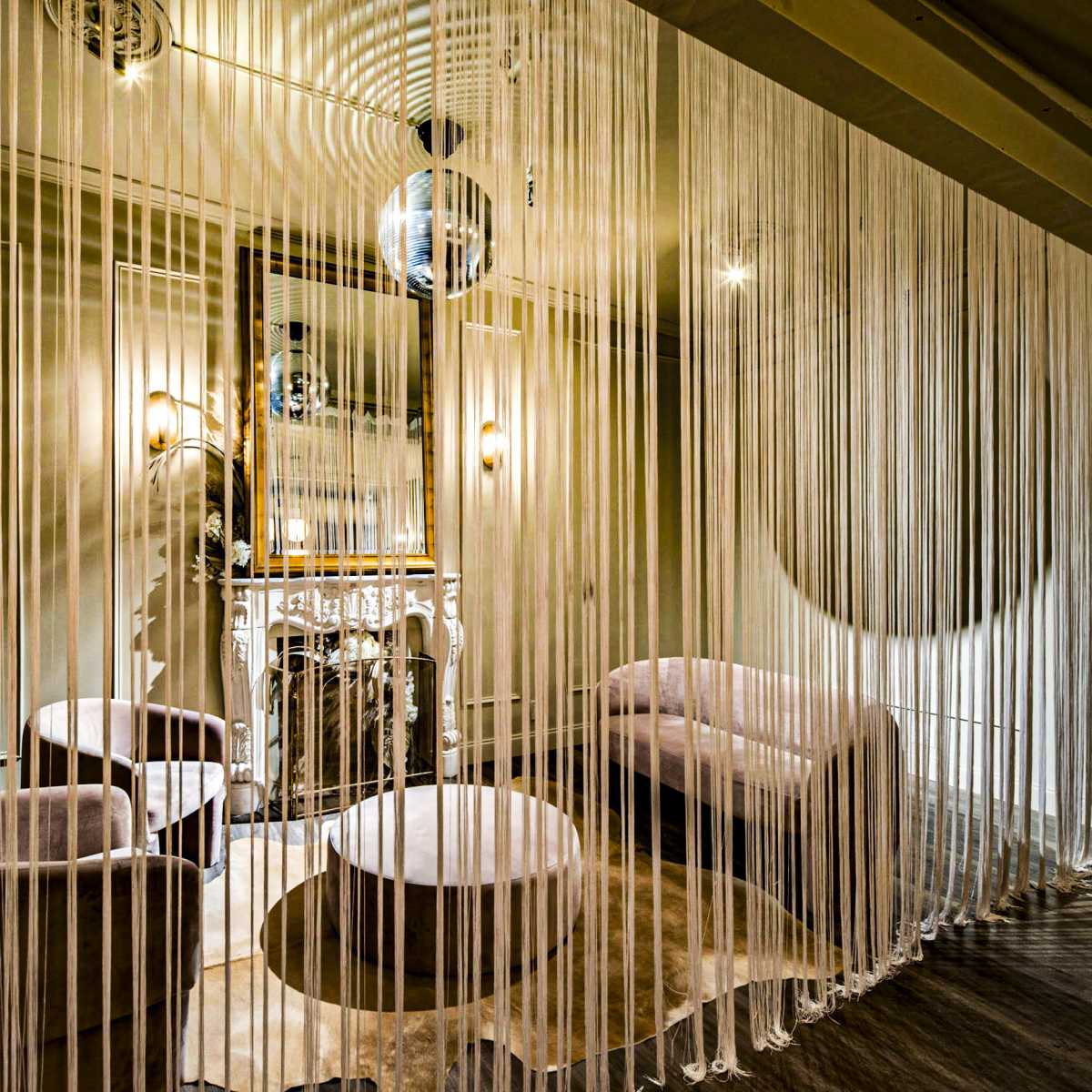 A stylish interior space with soft seating, a mirrored wall, and sheer curtains creating a partition.