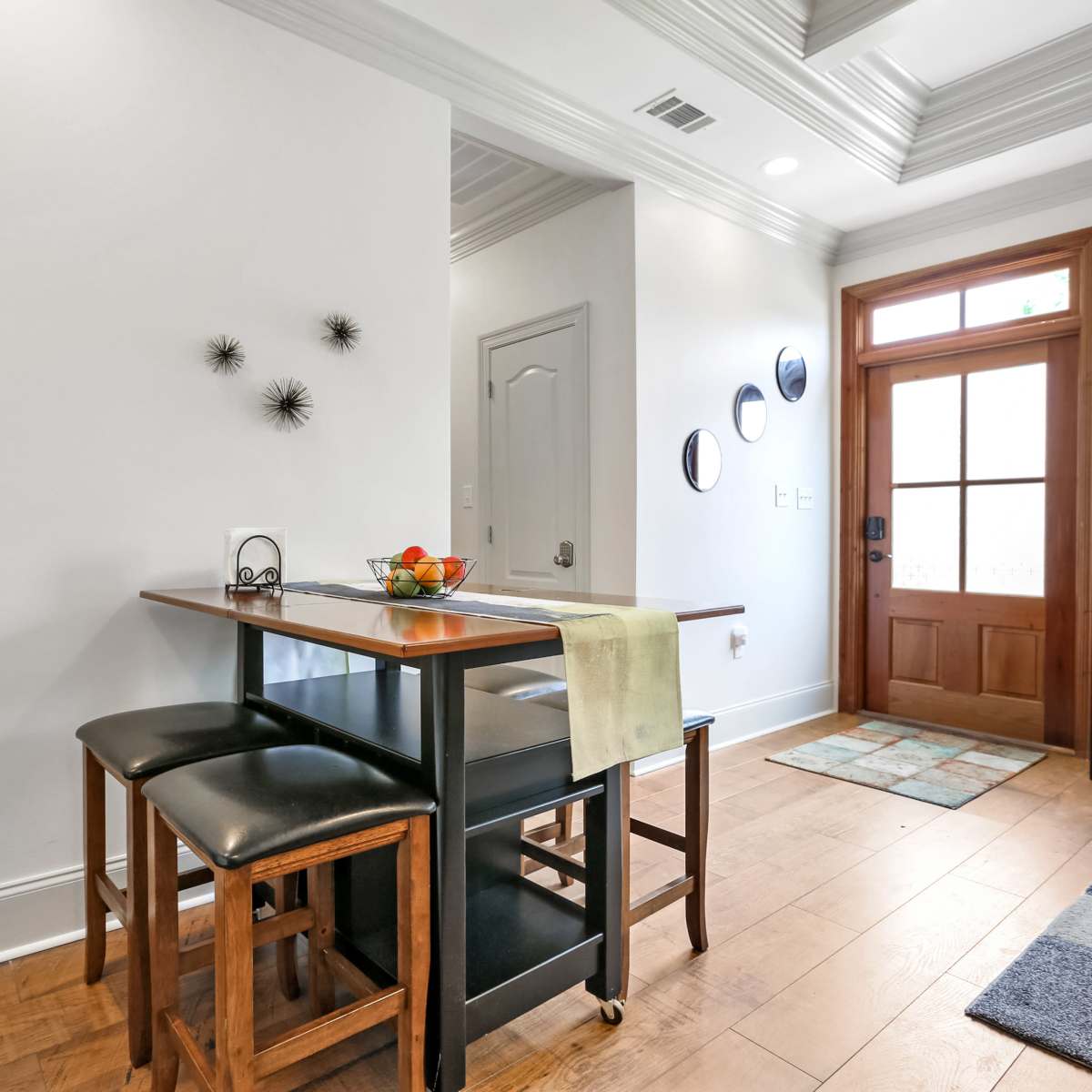 A modern kitchen area with a small table and two black stools, near a doorway with decorative circular wall art.