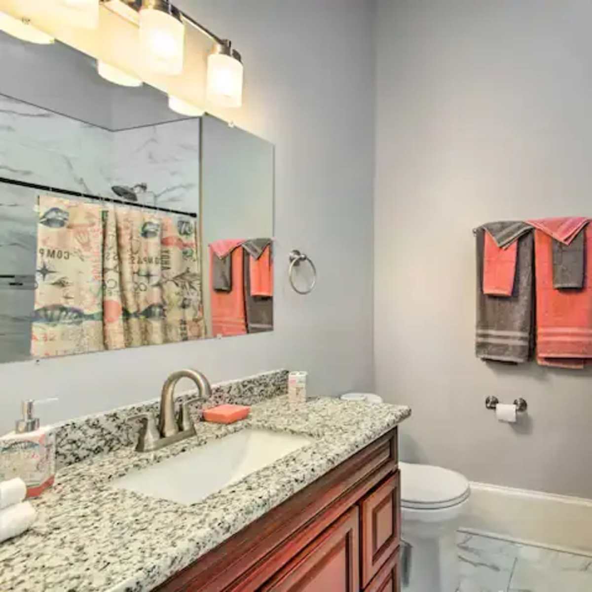 A bathroom featuring a granite countertop, a large mirror, a glass shower, and various towels hanging on a rack.