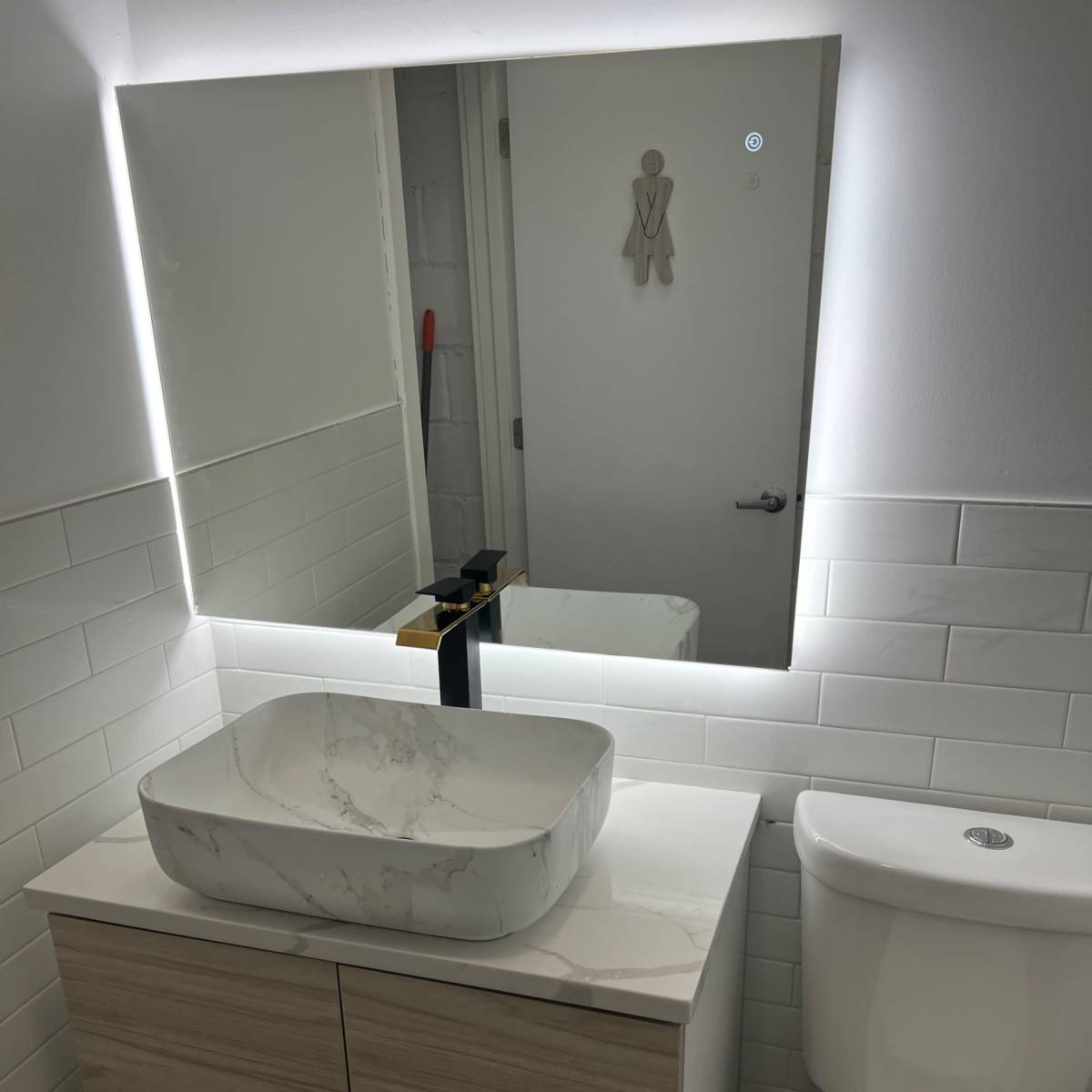 A modern bathroom features a wall-mounted mirror above a countertop with a marble vessel sink and a wooden vanity, alongside a white toilet.