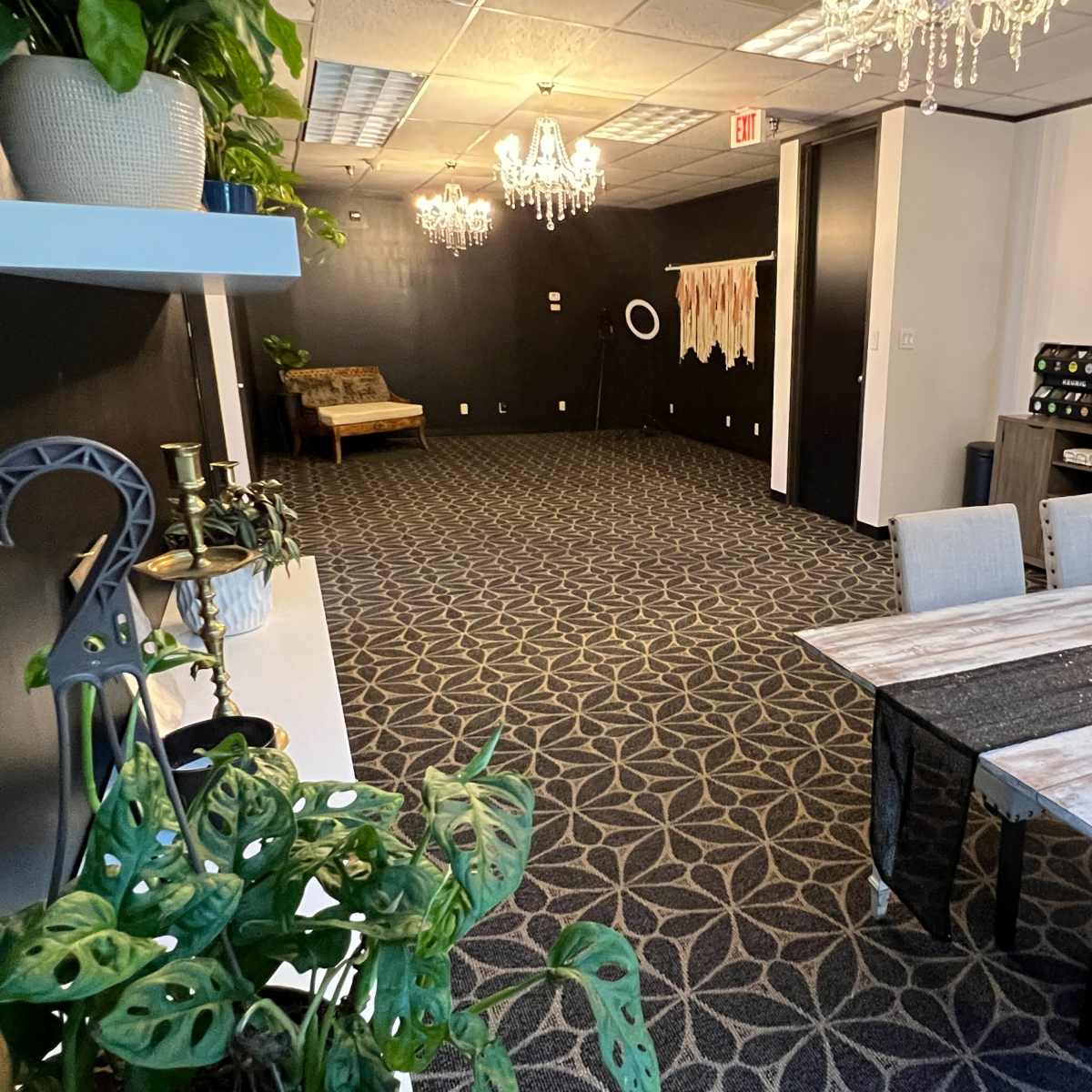 A spacious room with a patterned carpet, a dining table with chairs, and decorative elements like chandeliers and plants.