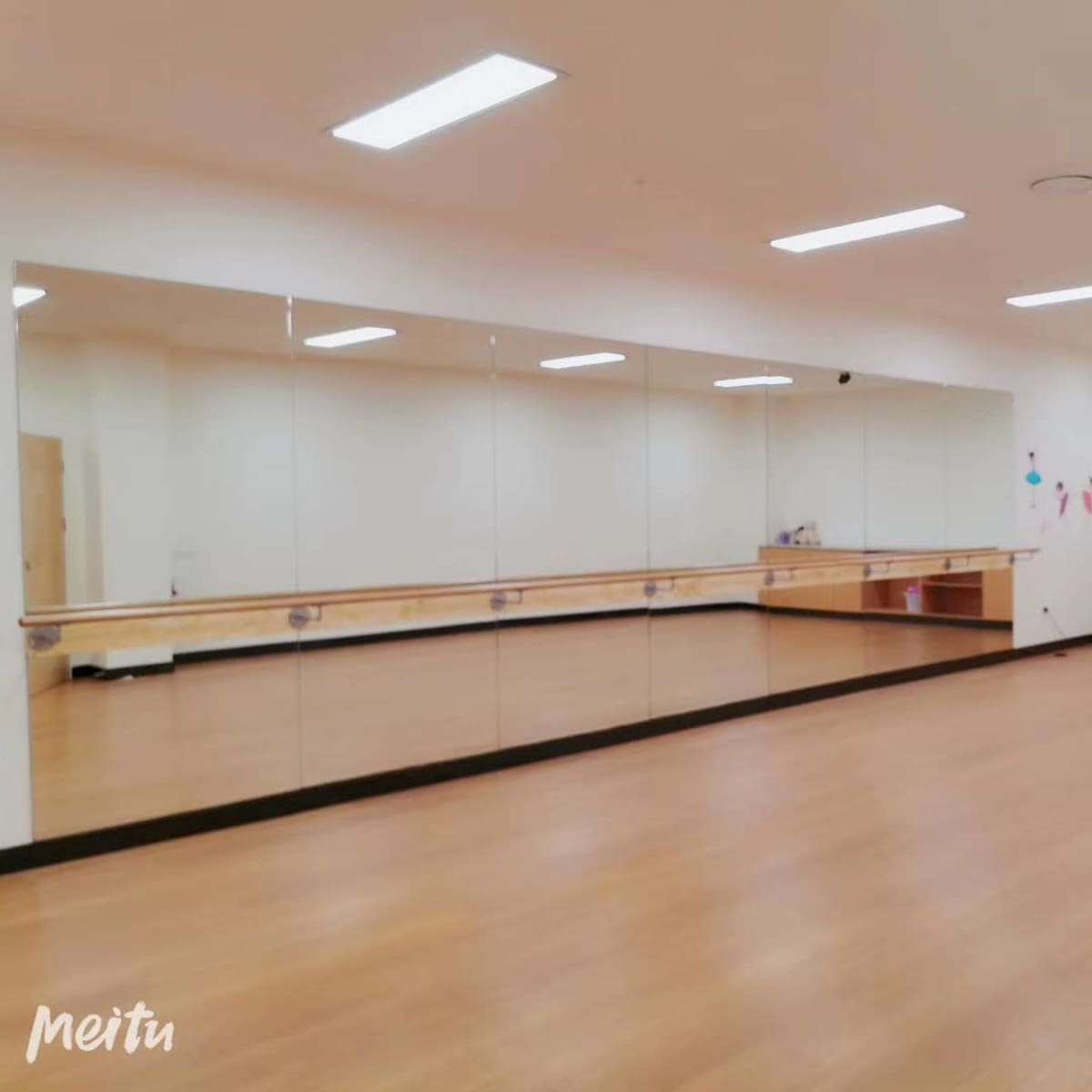 A bright, empty dance studio with large mirrors on one wall and wooden flooring.