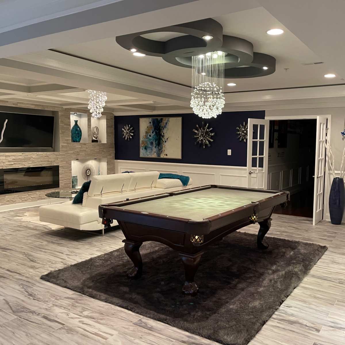 A spacious, modern game room featuring a billiard table at center, surrounded by stylish decor, including a sectional sofa and decorative vases.