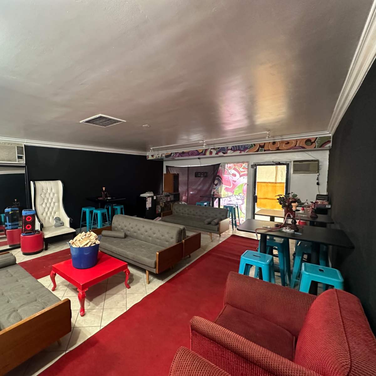 The room features several seating areas with gray sofas and a red carpet, alongside a table with popcorn in the center.
