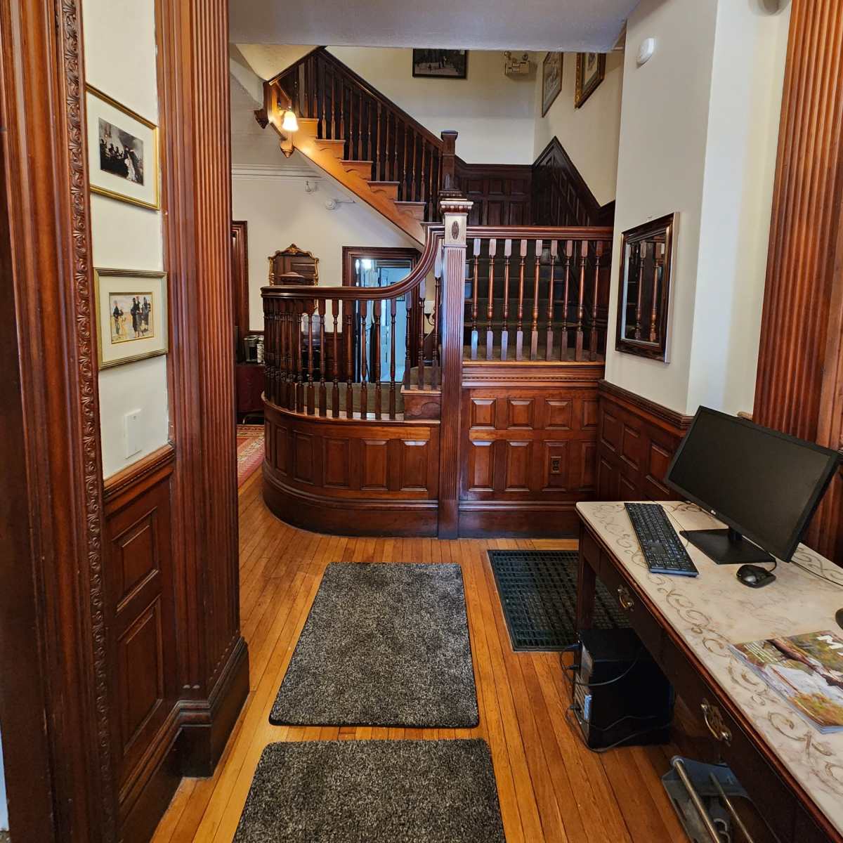 A wooden entryway leading to a staircase with a curved railing, flanked by dark wood paneling and decorative frames on the walls.