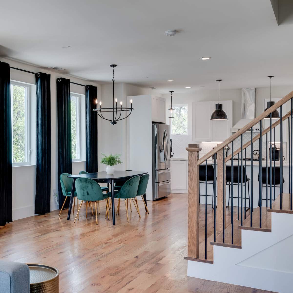 A modern open-concept living space featuring a dining area with a round table and chairs, a kitchen with white cabinetry, and a staircase leading to an upper level.