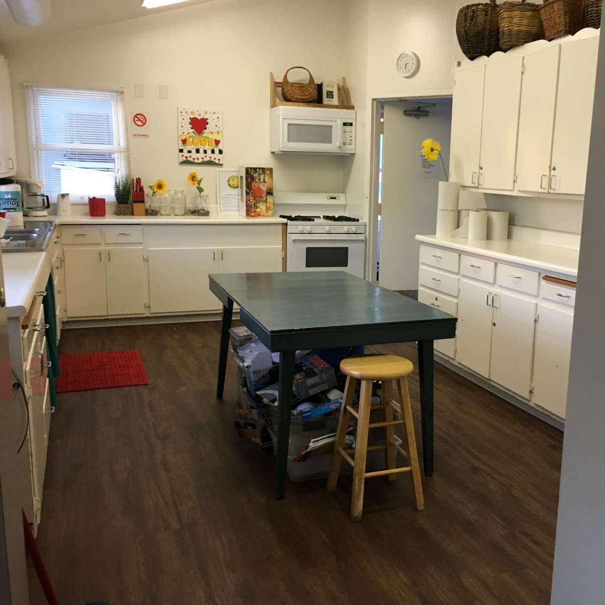 A kitchen featuring white cabinets, a central green table with a stool, and various appliances.