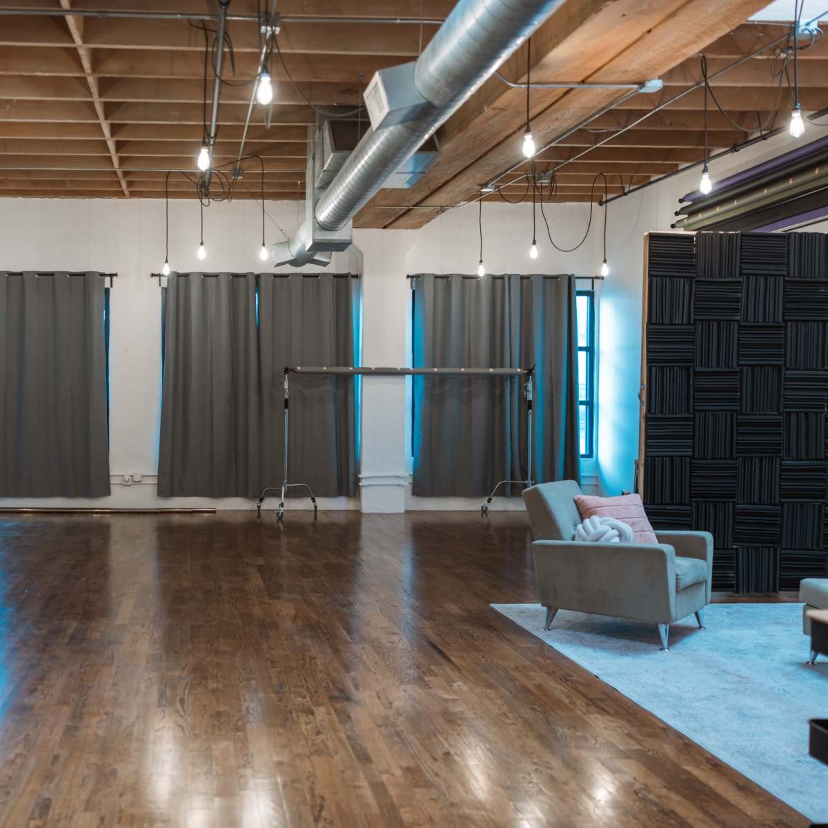 A spacious, well-lit studio with wooden flooring, gray curtains, and a vibrant orange wall.