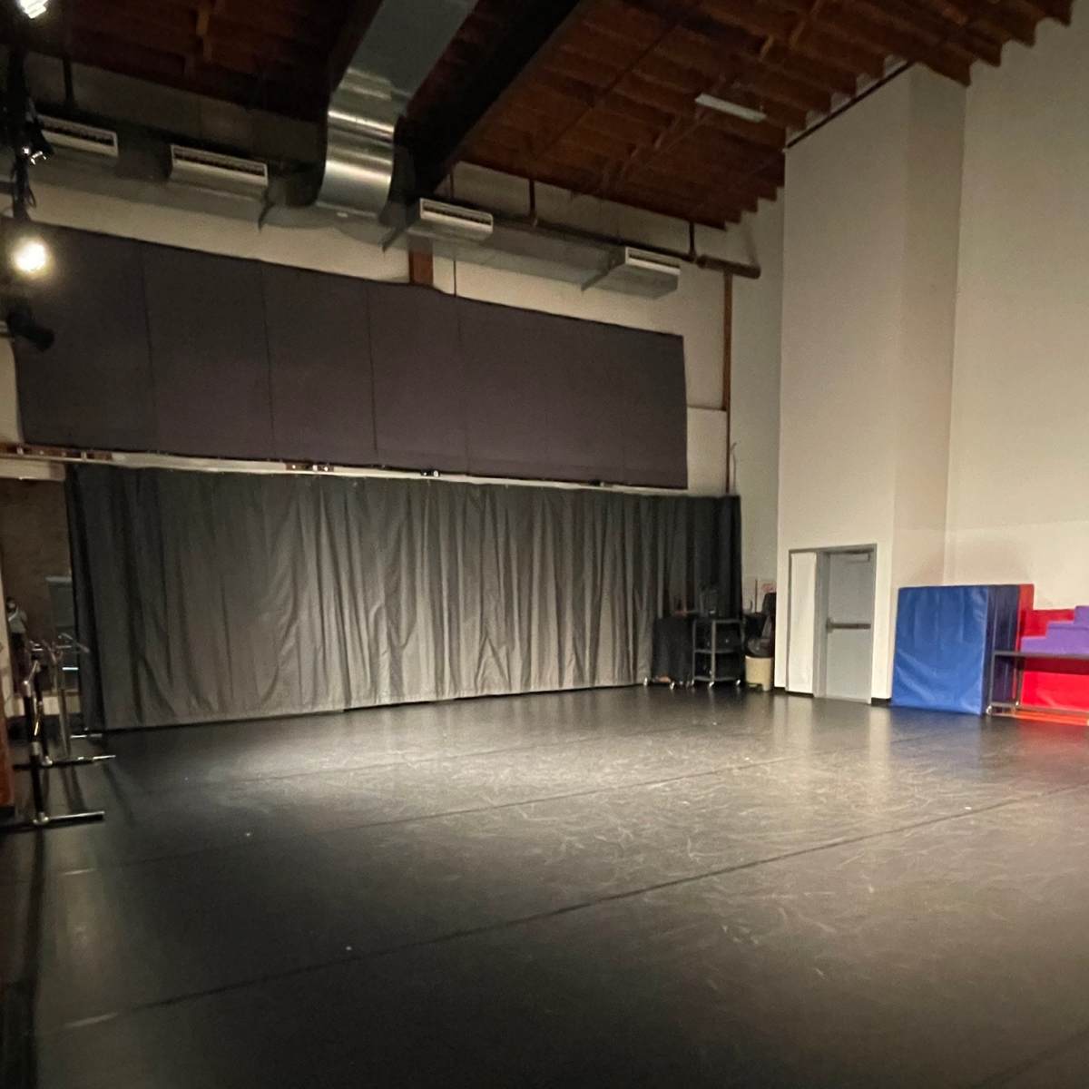 A dimly lit dance studio with a black floor and curtains along one wall.