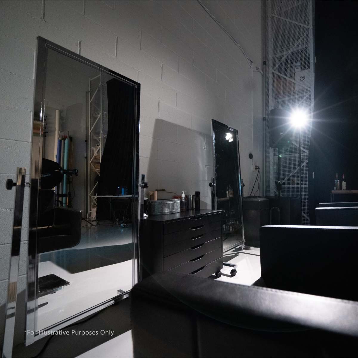 A dimly lit room with two large mirrors, black chairs, and a spotlight directed at the corner.