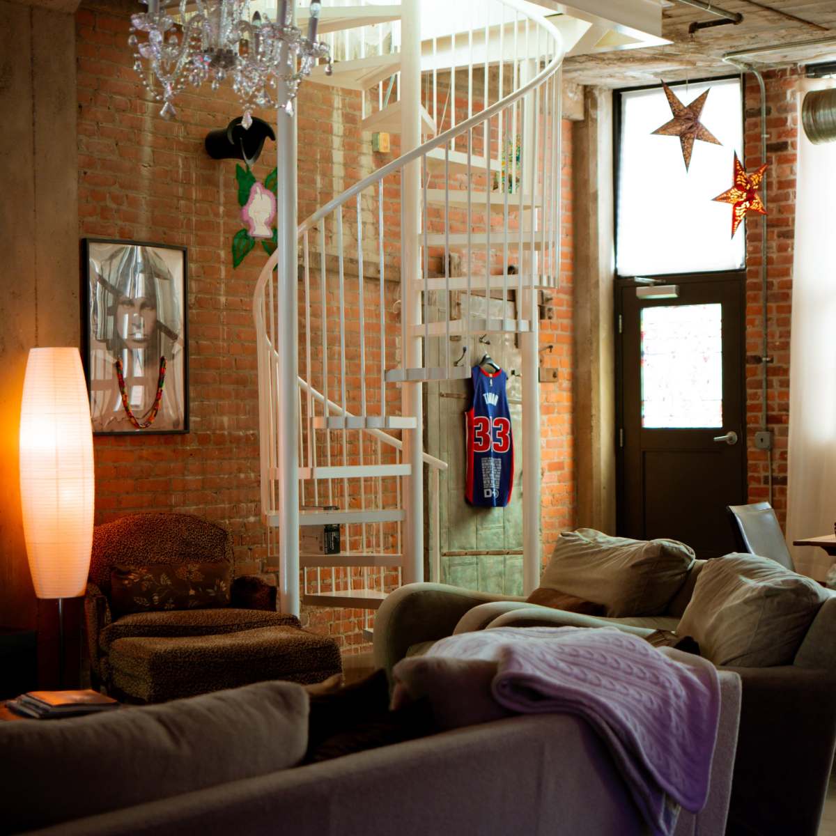 A modern living space with exposed brick walls, a spiral staircase, and distinct lighting fixtures.