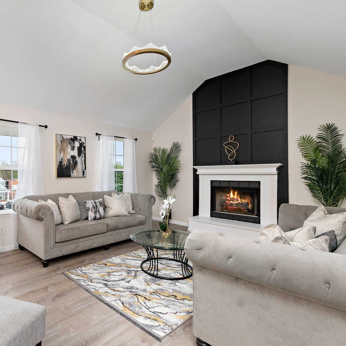A cozy living room features a fireplace, a gray sectional sofa, and large windows with sheer curtains.