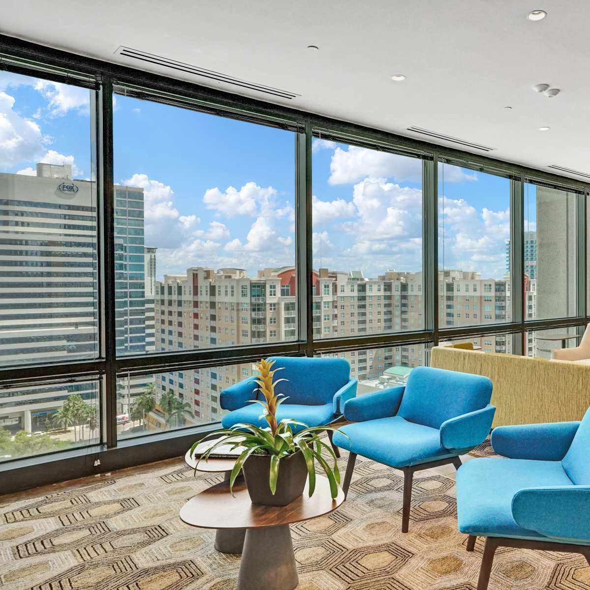 A modern office lounge with colorful chairs, a coffee table, and large windows overlooking a cityscape.