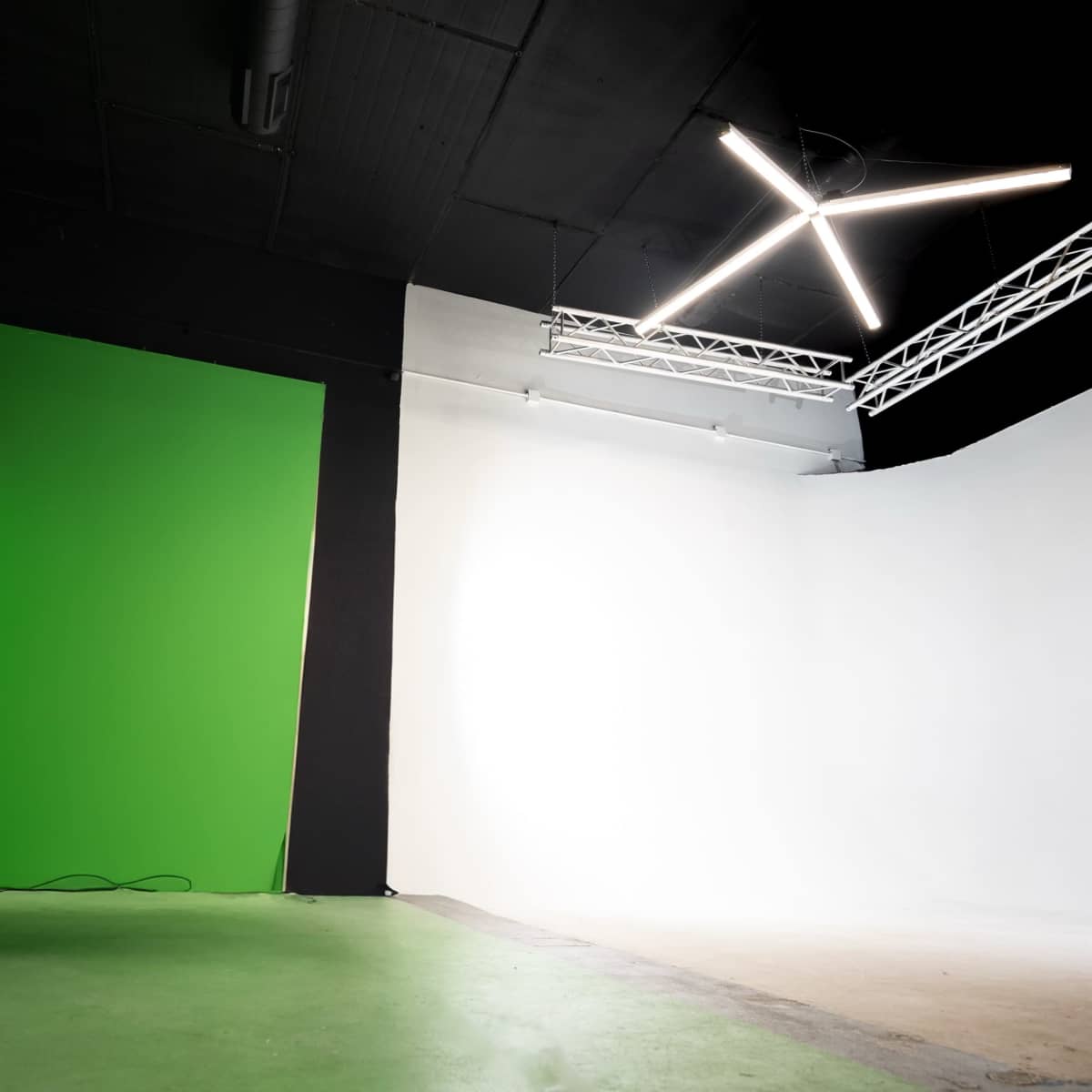 A studio space featuring a green screen on one wall and a white backdrop on the opposite side, illuminated by overhead lights.