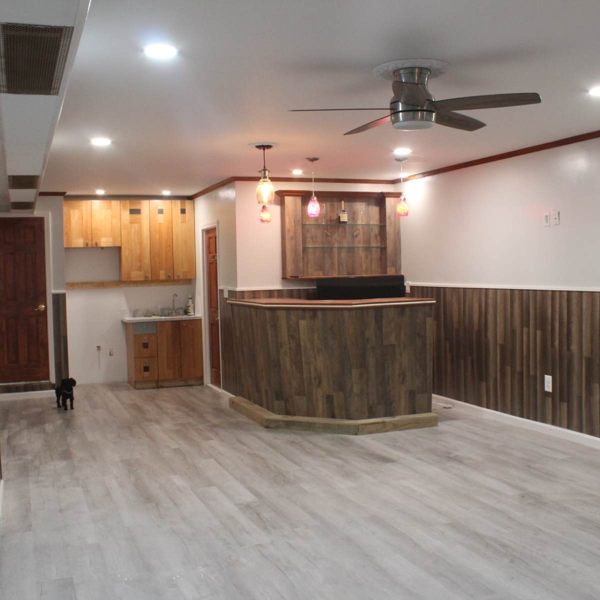 A spacious, modern room featuring a wooden bar area with pendant lighting and laminate flooring.