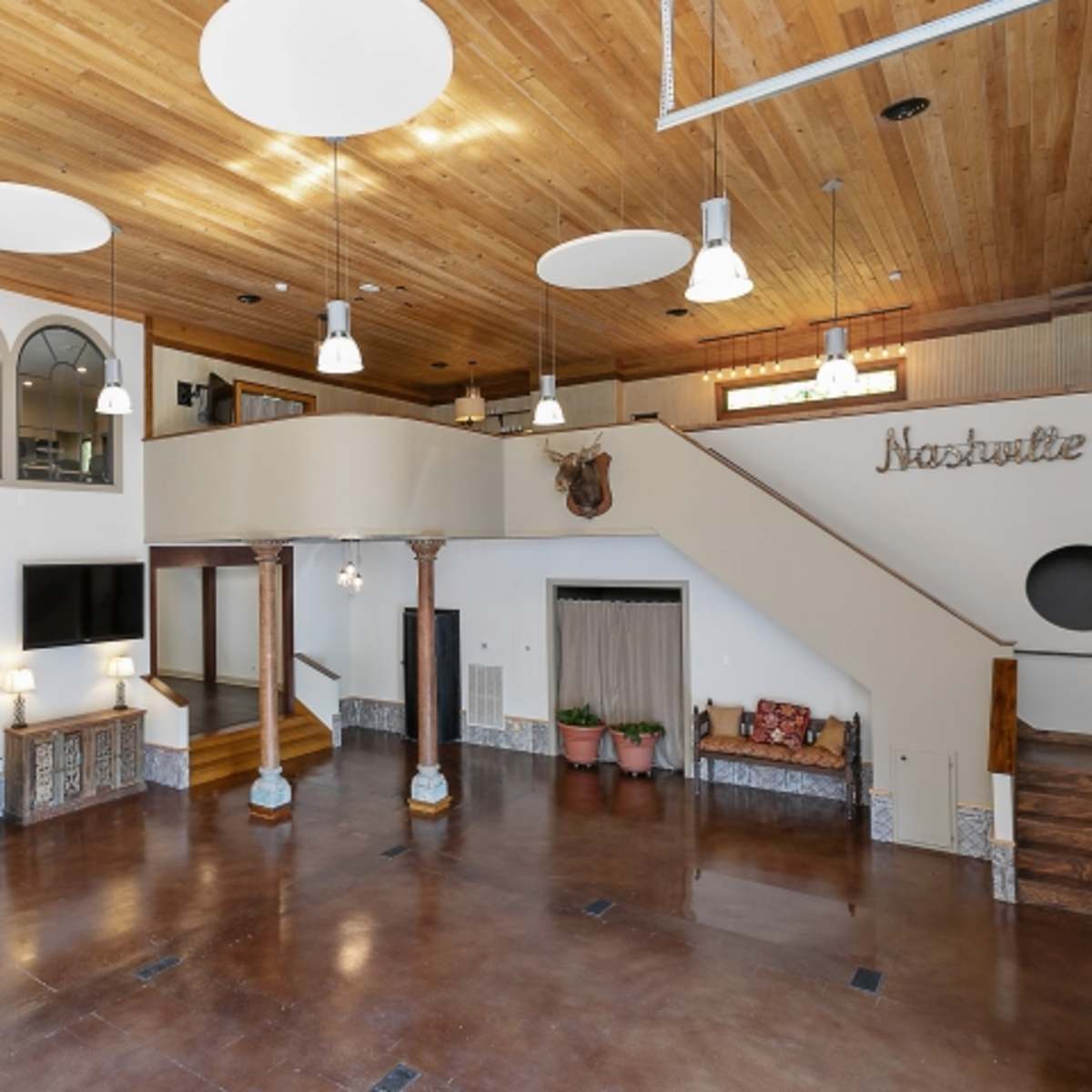An open, spacious interior with a wooden ceiling, large windows, and a staircase leading to a second level.