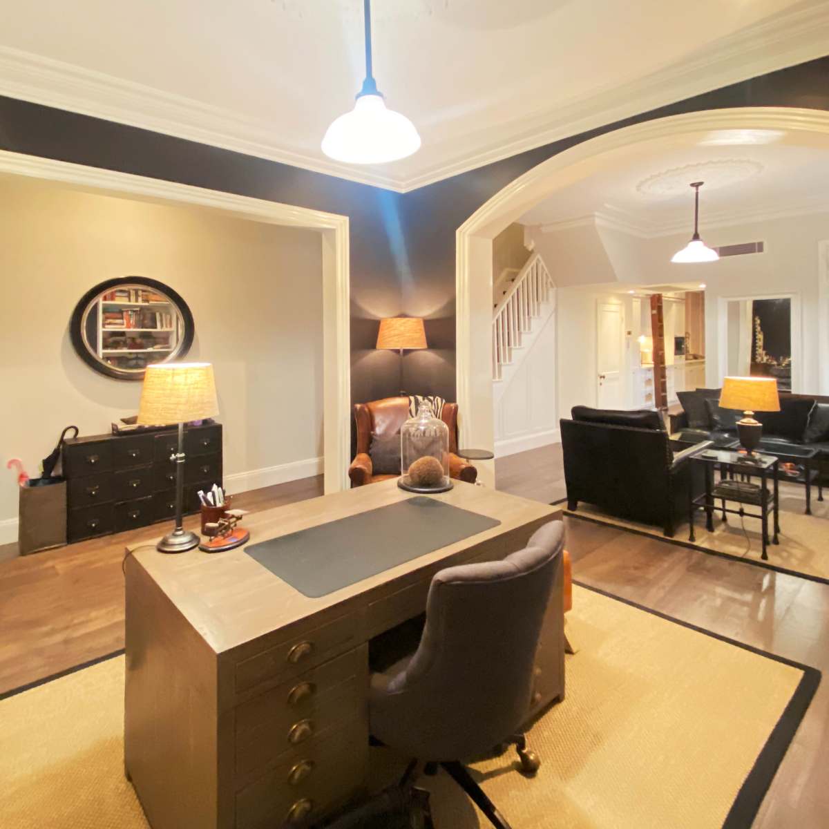 An elegantly designed office space featuring a wooden desk, two armchairs, and a staircase leading to another area.