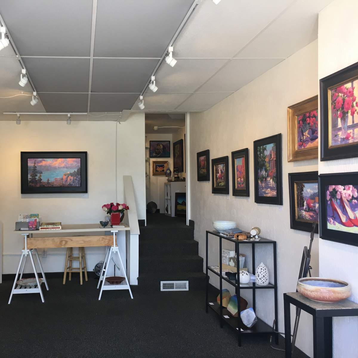 The interior of an art gallery featuring framed paintings on the walls, display cases with jewelry, and various artistic items throughout the space.