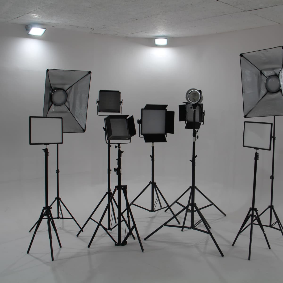A set of studio lighting equipment arranged on tripods in a plain white room.