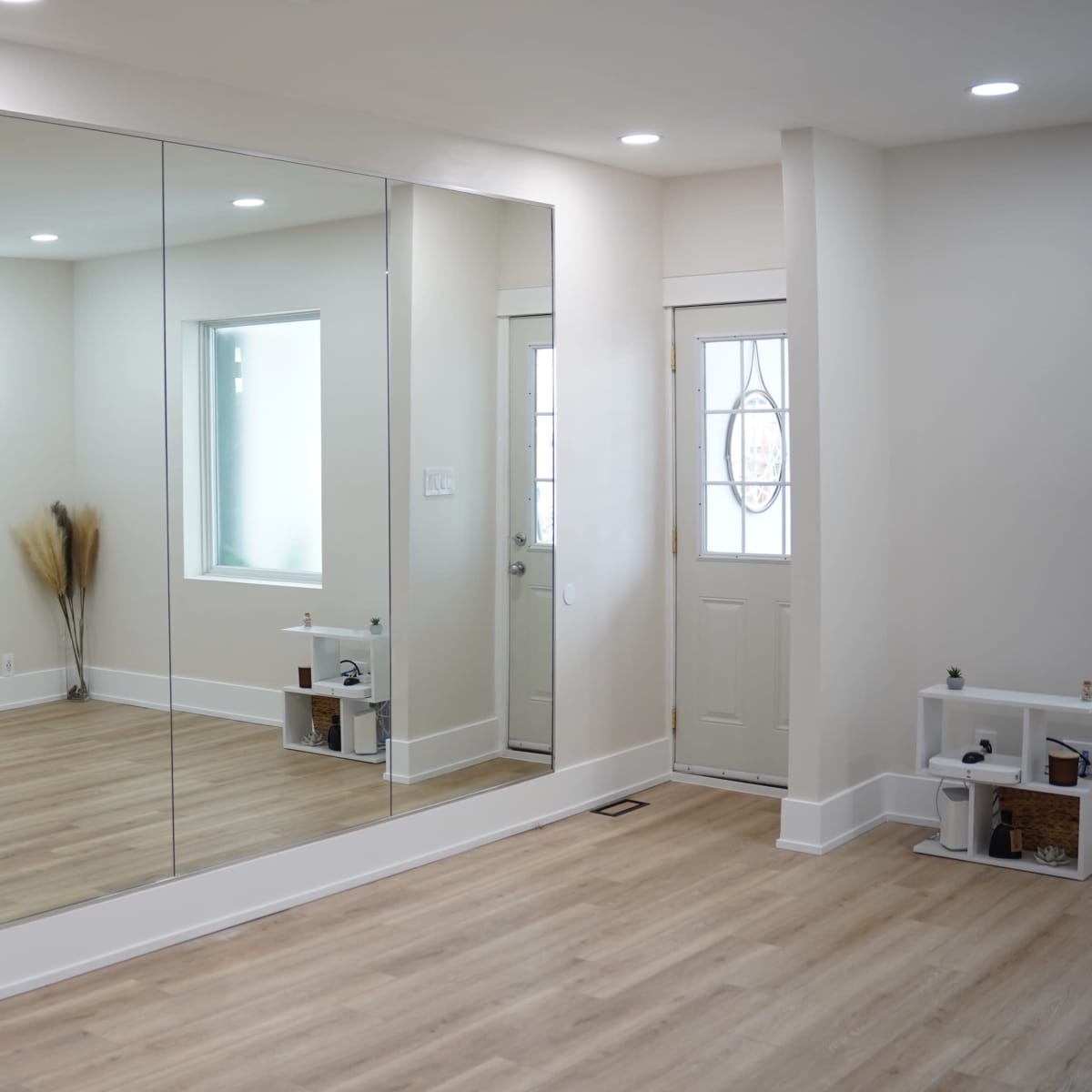 A spacious room features a large mirrored wall, a small television mounted on the opposite wall, and a front door with a window beside it.
