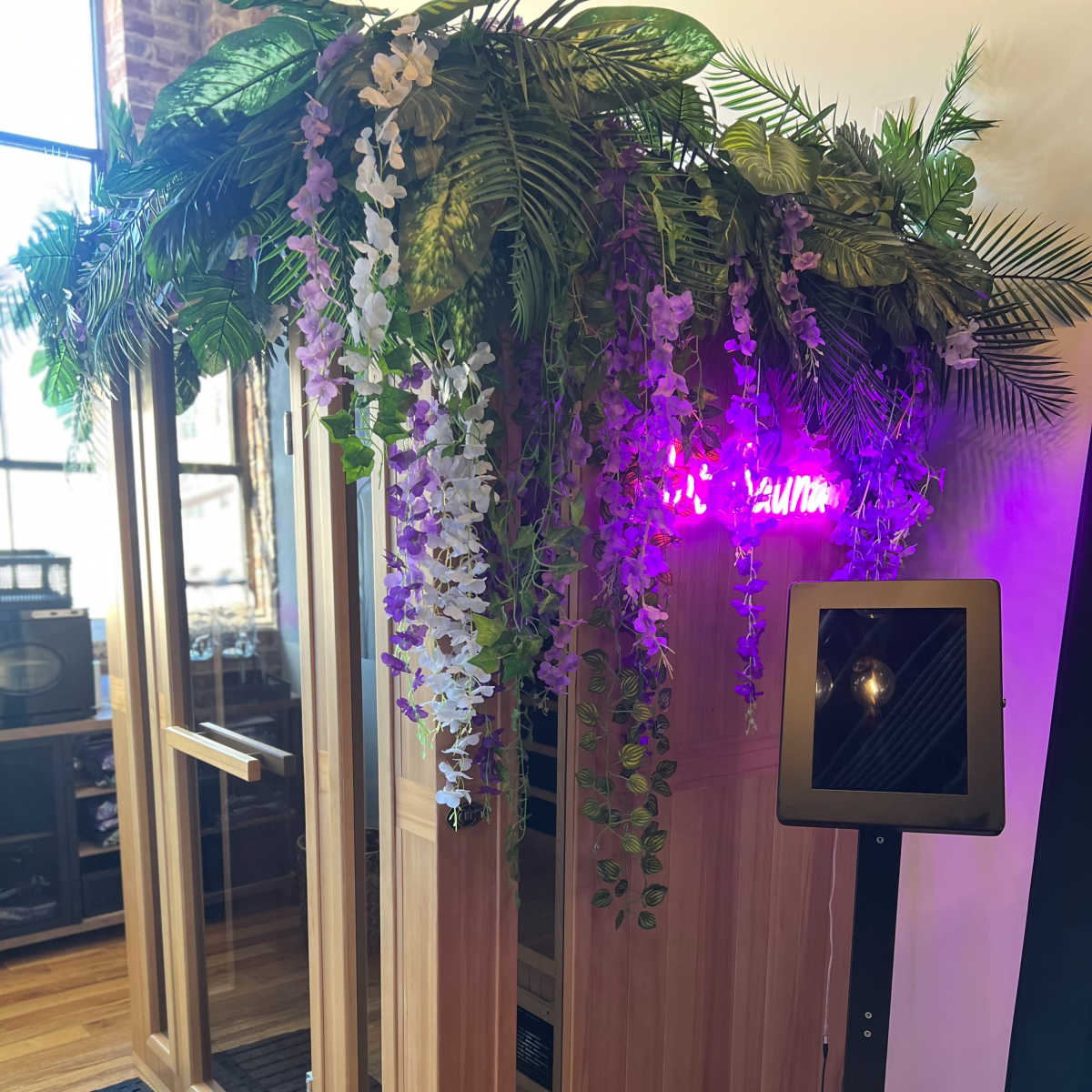 A wooden sauna with a floral decoration on top and a tablet stand beside it.