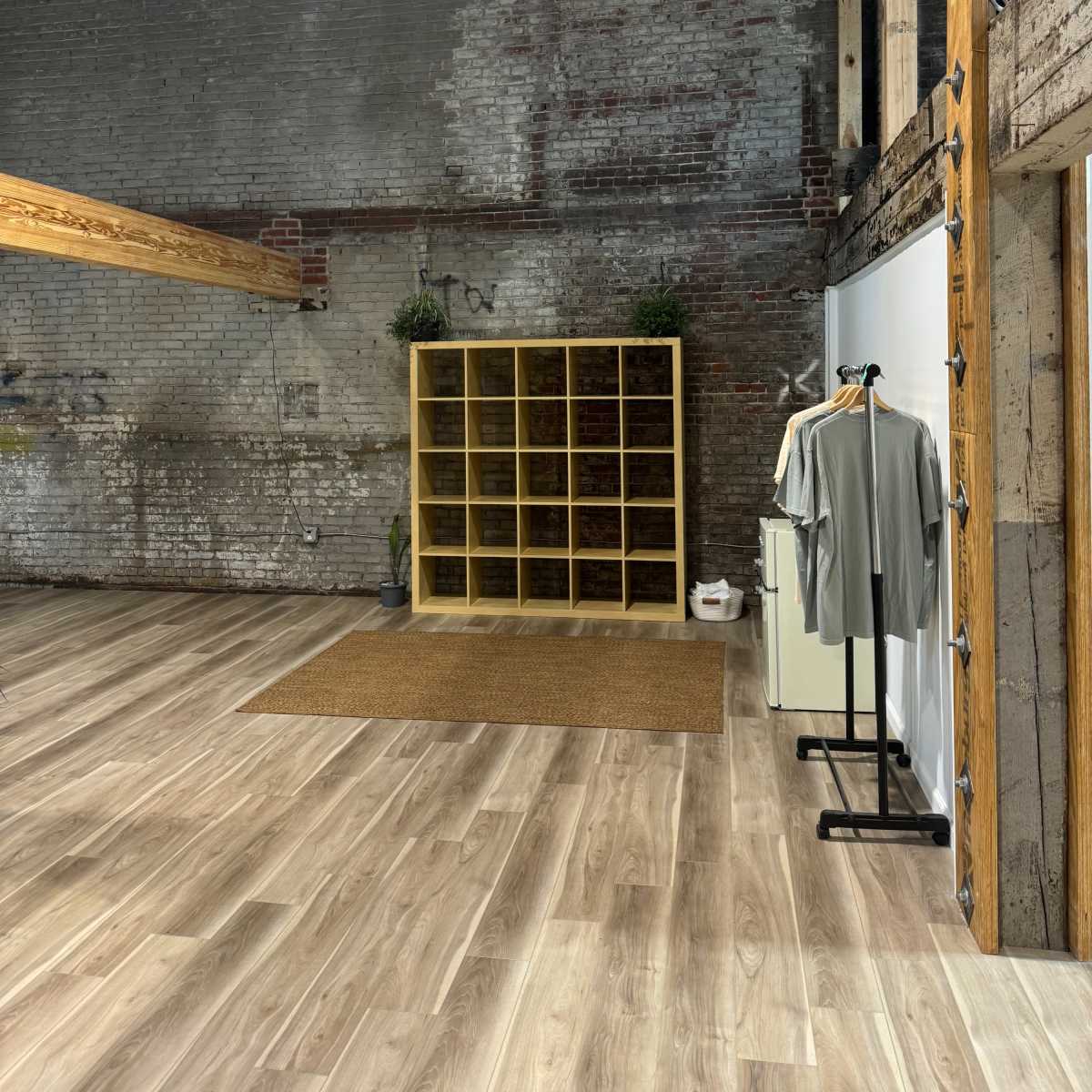 An industrial-style interior with exposed brick walls, wooden beams, a shelving unit, and a clothing rack.