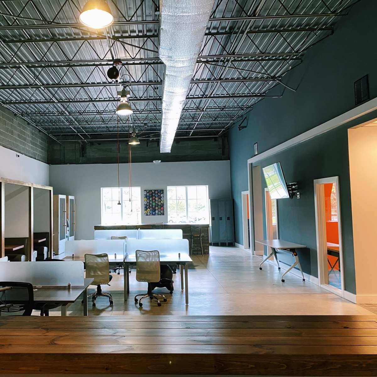 A spacious office interior with desks and chairs arranged under high ceilings, featuring large windows and colorful accent walls.