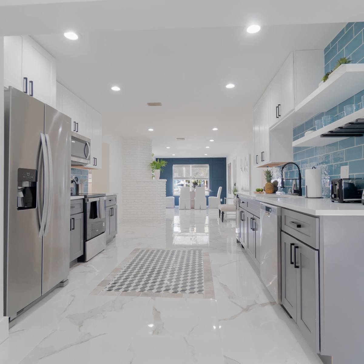 A modern kitchen with stainless steel appliances, white cabinetry, and blue tiled backsplash, featuring a marble floor and open layout.