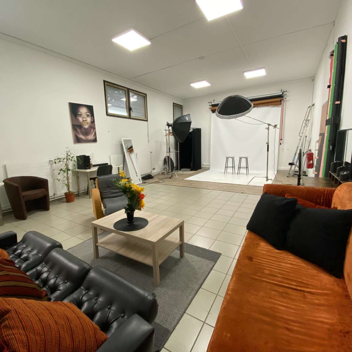 A spacious photography studio furnished with a seating area, a table with flowers, and a backdrop setup for photo shoots.
