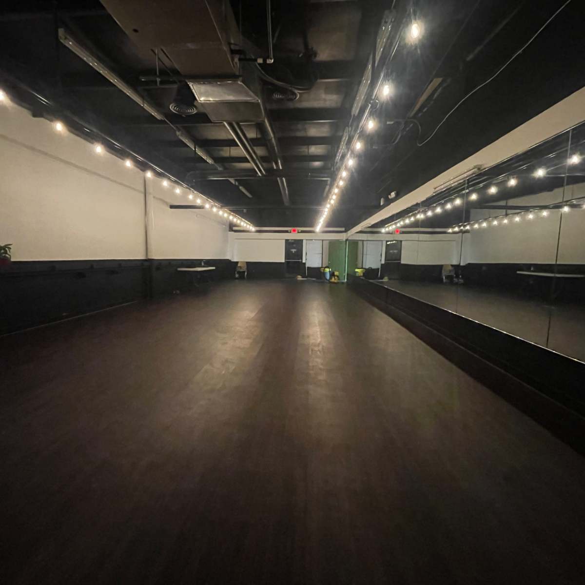 An empty dance studio with a mirrored wall and bright overhead lights.