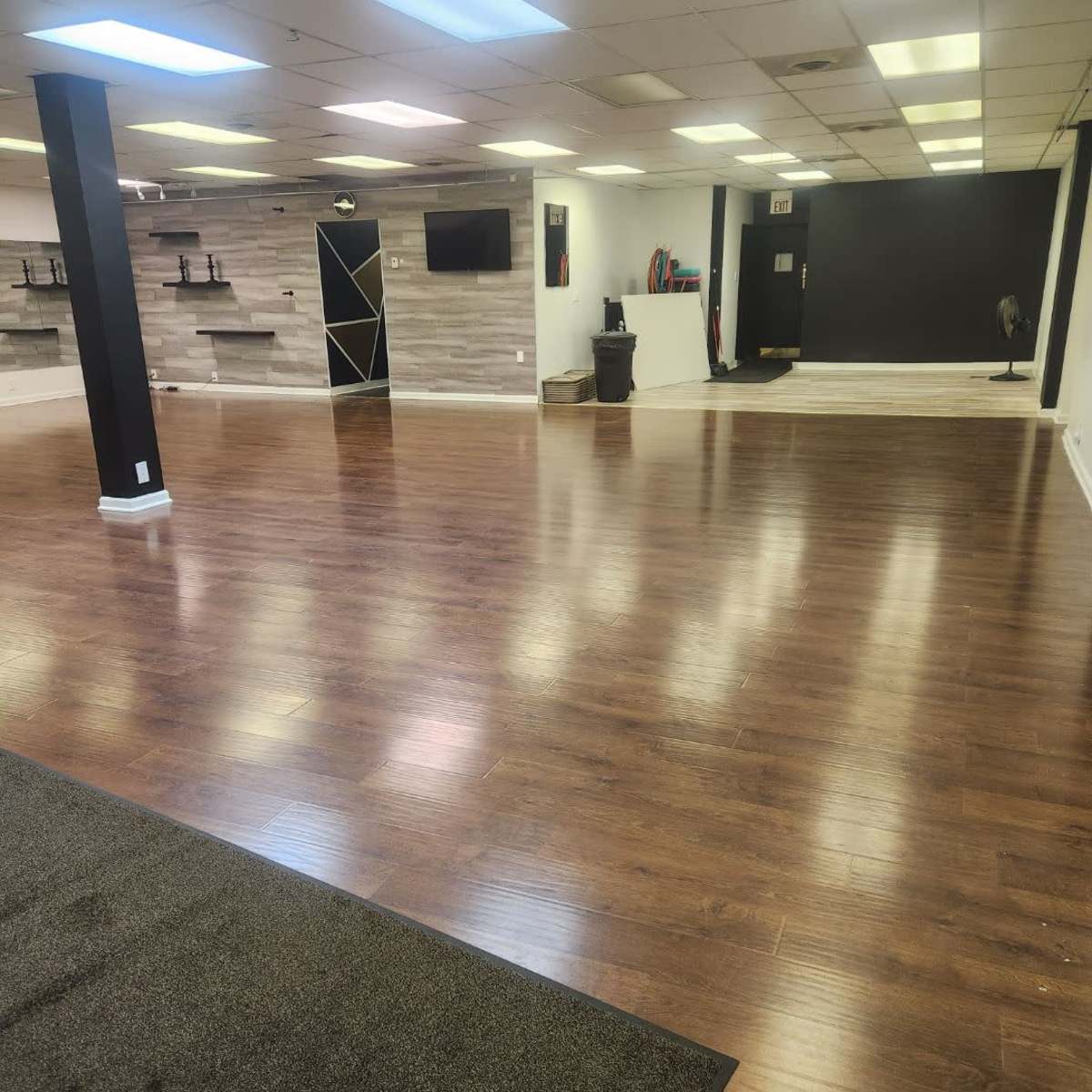A spacious, empty room with wooden flooring, distinct sections of wall, and a few furnishings along the sides.