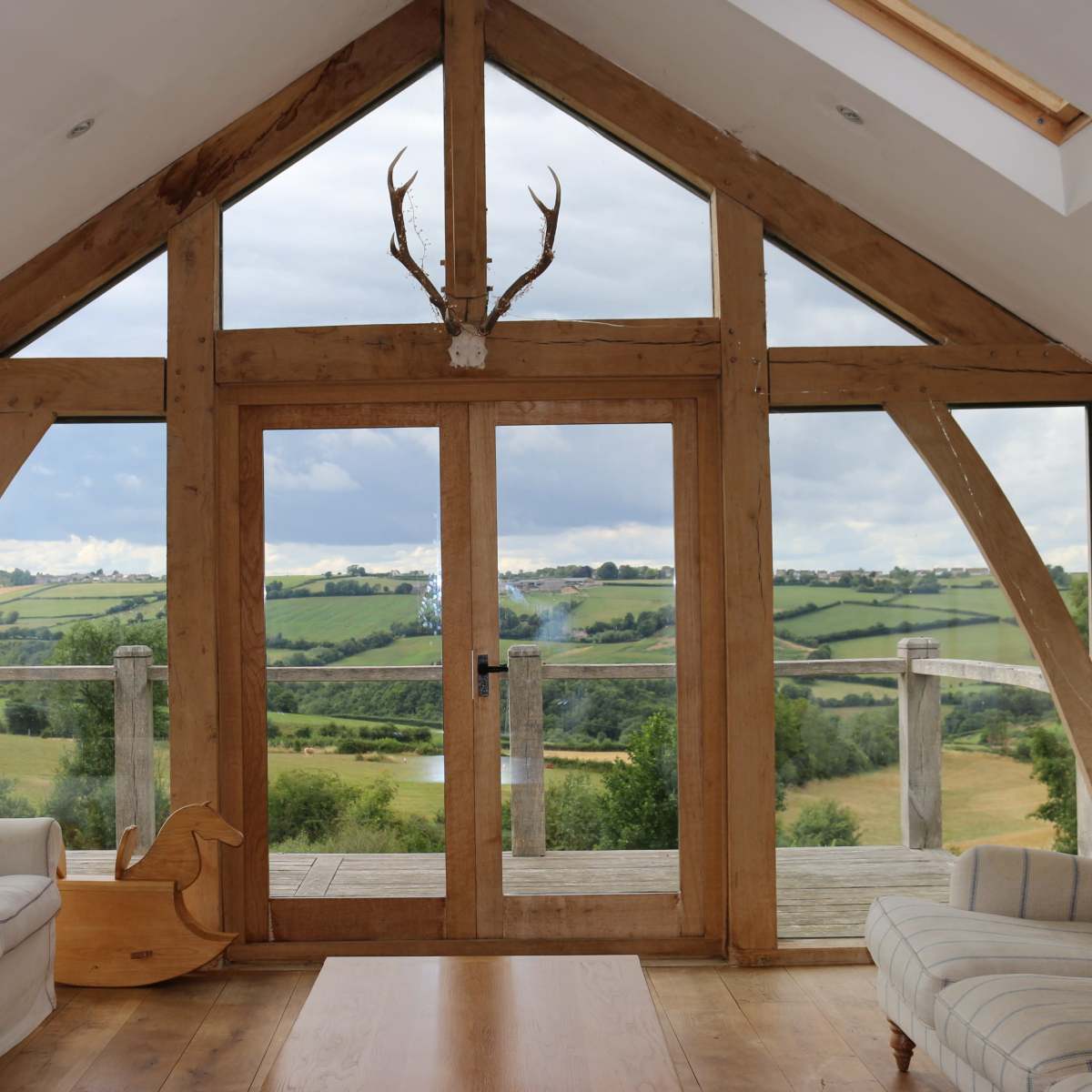 A wooden-framed room features large glass doors opening to a view of rolling green hills.