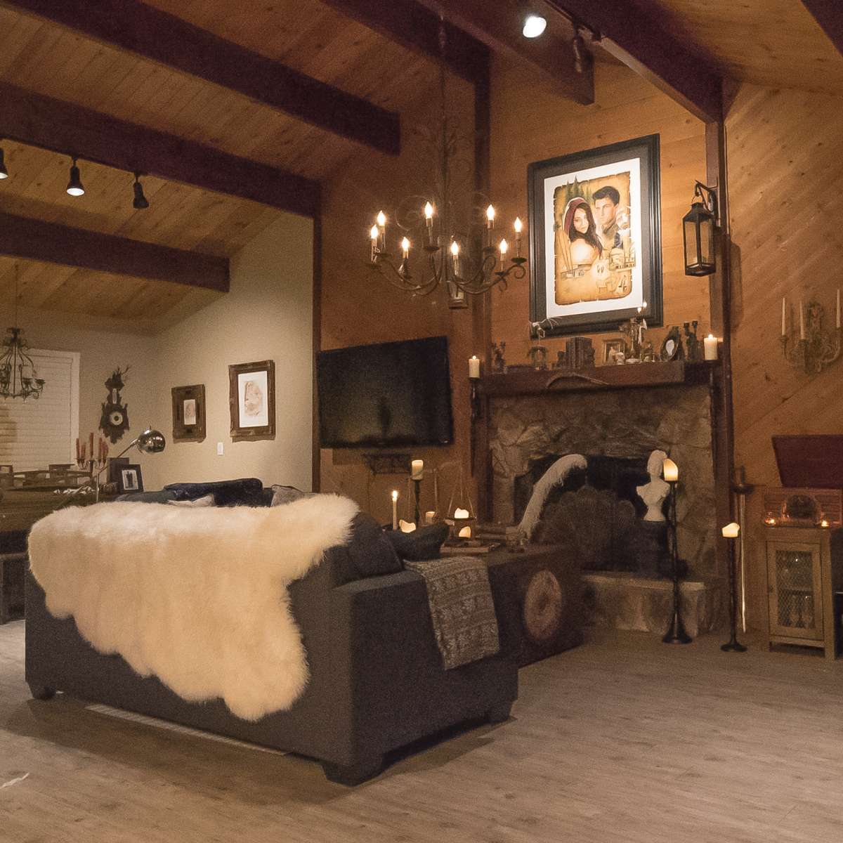 The scene features a cozy living room with rustic wooden beams, a stone fireplace adorned with candles, and a large fur throw draped over a dark sofa.
