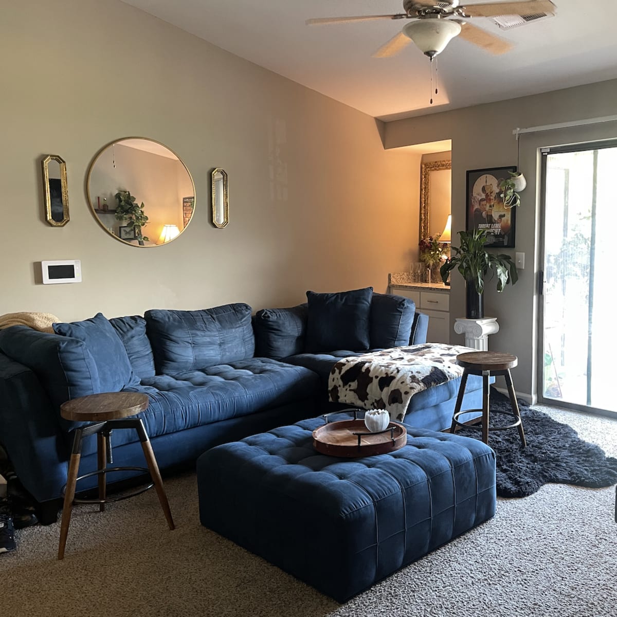 The living room features a blue sectional sofa, a matching ottoman, and a sliding glass door leading to a patio.