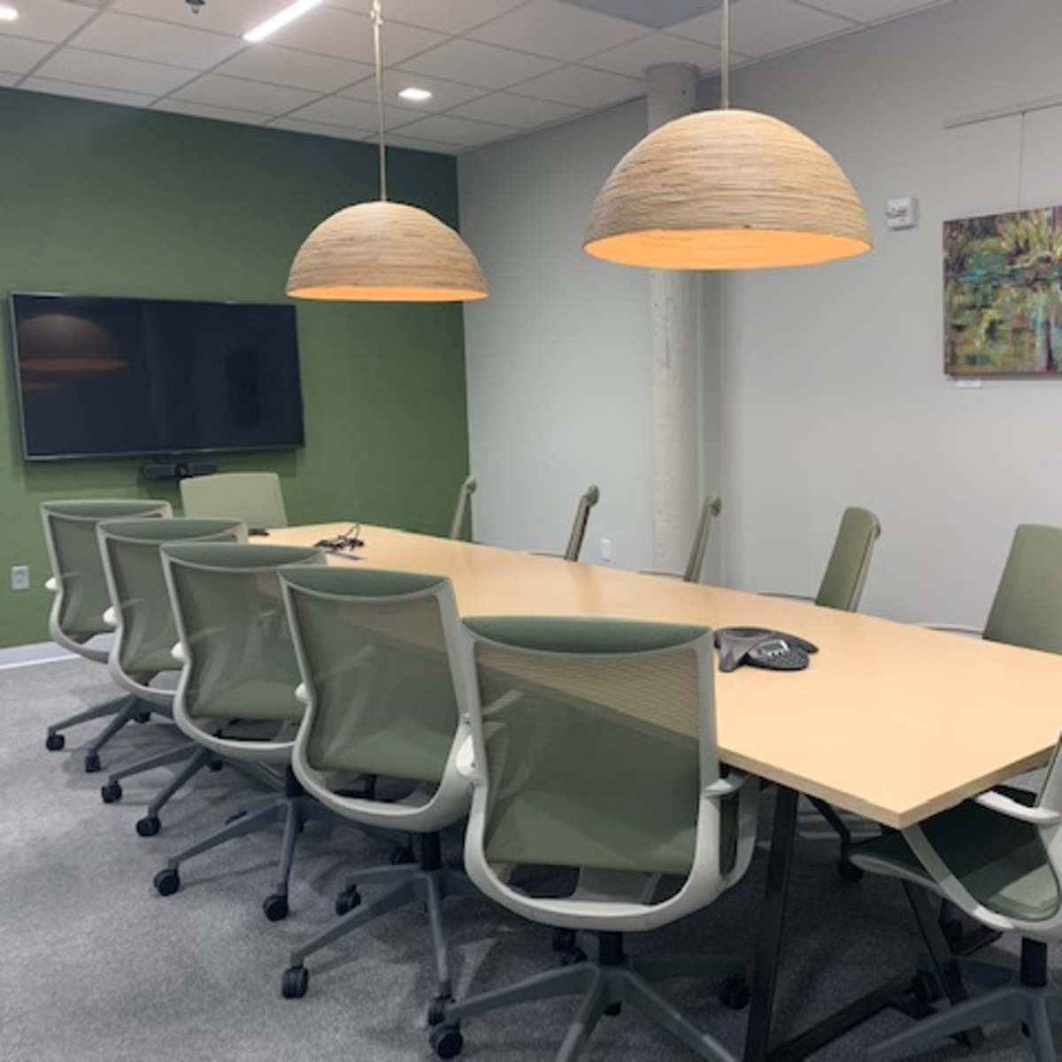 A conference room with a long table, green chairs, and two pendant lights hanging above it.