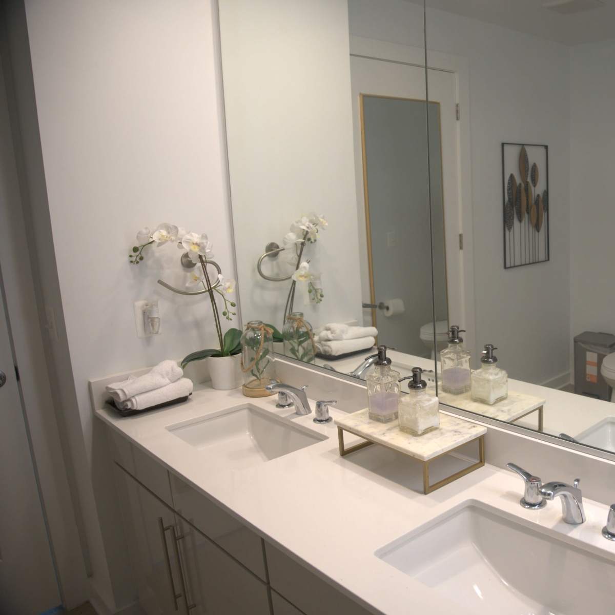 A modern bathroom with a double sink vanity, a large mirror, and a shower area visible in the background.