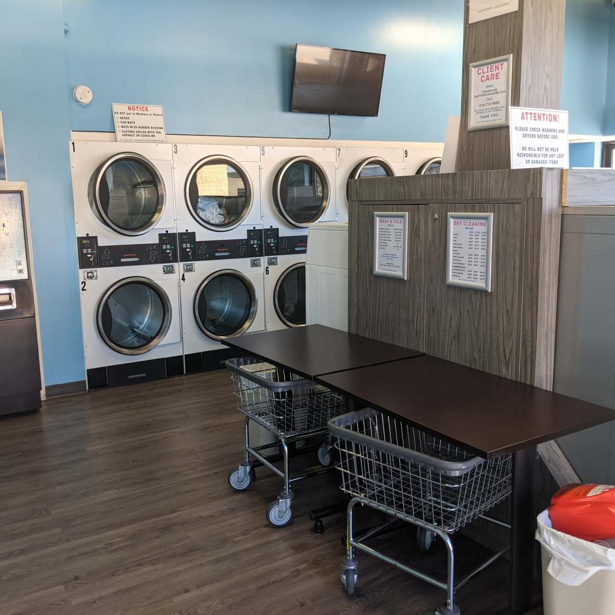 A laundromat interior with washing machines, tables, and laundry carts against a blue wall.