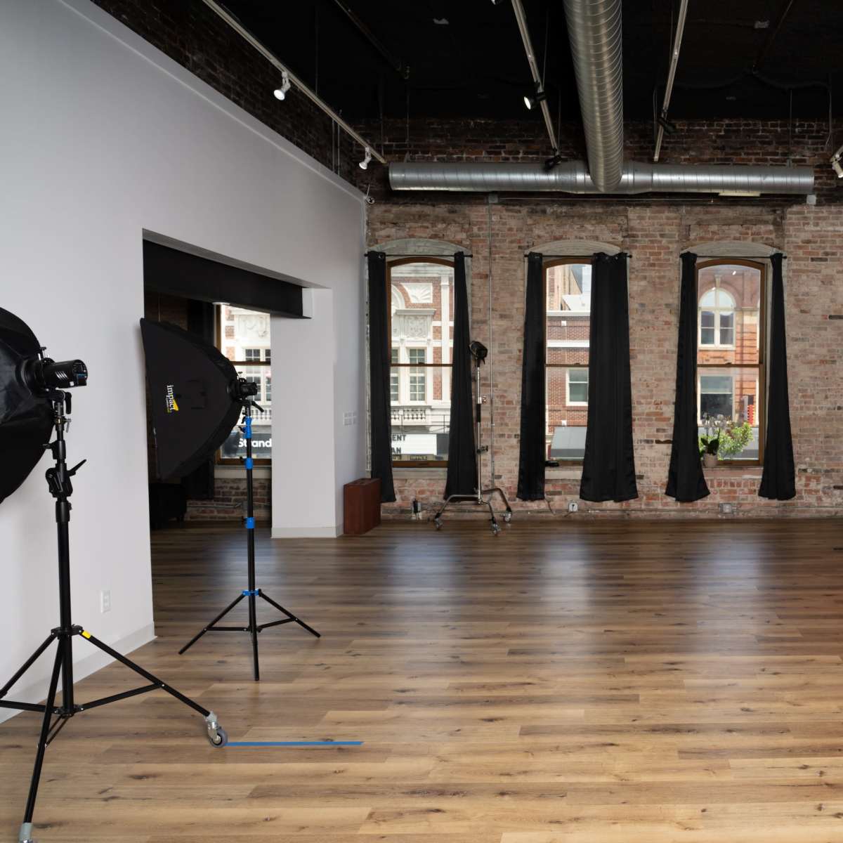 A spacious, empty photography studio with large windows, a red backdrop, and lighting equipment set up in the room.