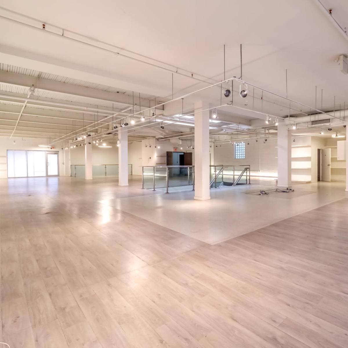 A spacious, empty commercial area with light-colored flooring, white walls, and large windows allowing natural light to fill the space.