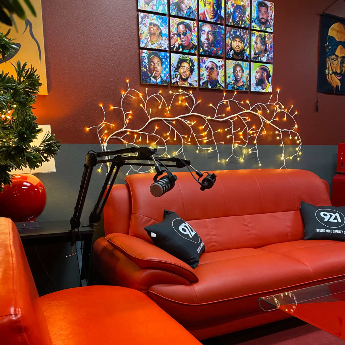 A modern lounge area with orange leather sofas, a glass coffee table, and decorative fairy lights above a collection of portraits on the wall.