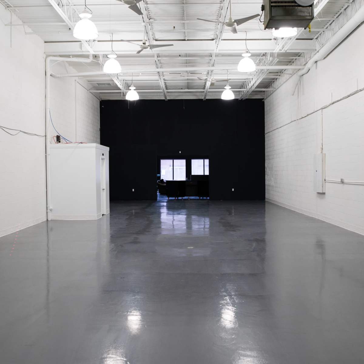 A spacious, empty room with gray floors, white walls, and a black wall at the far end, featuring a large window.