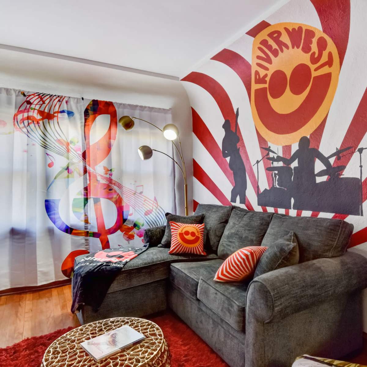 A vibrant living room featuring a gray sofa, colorful wall murals of musical notes and figures, and a decorative rug.