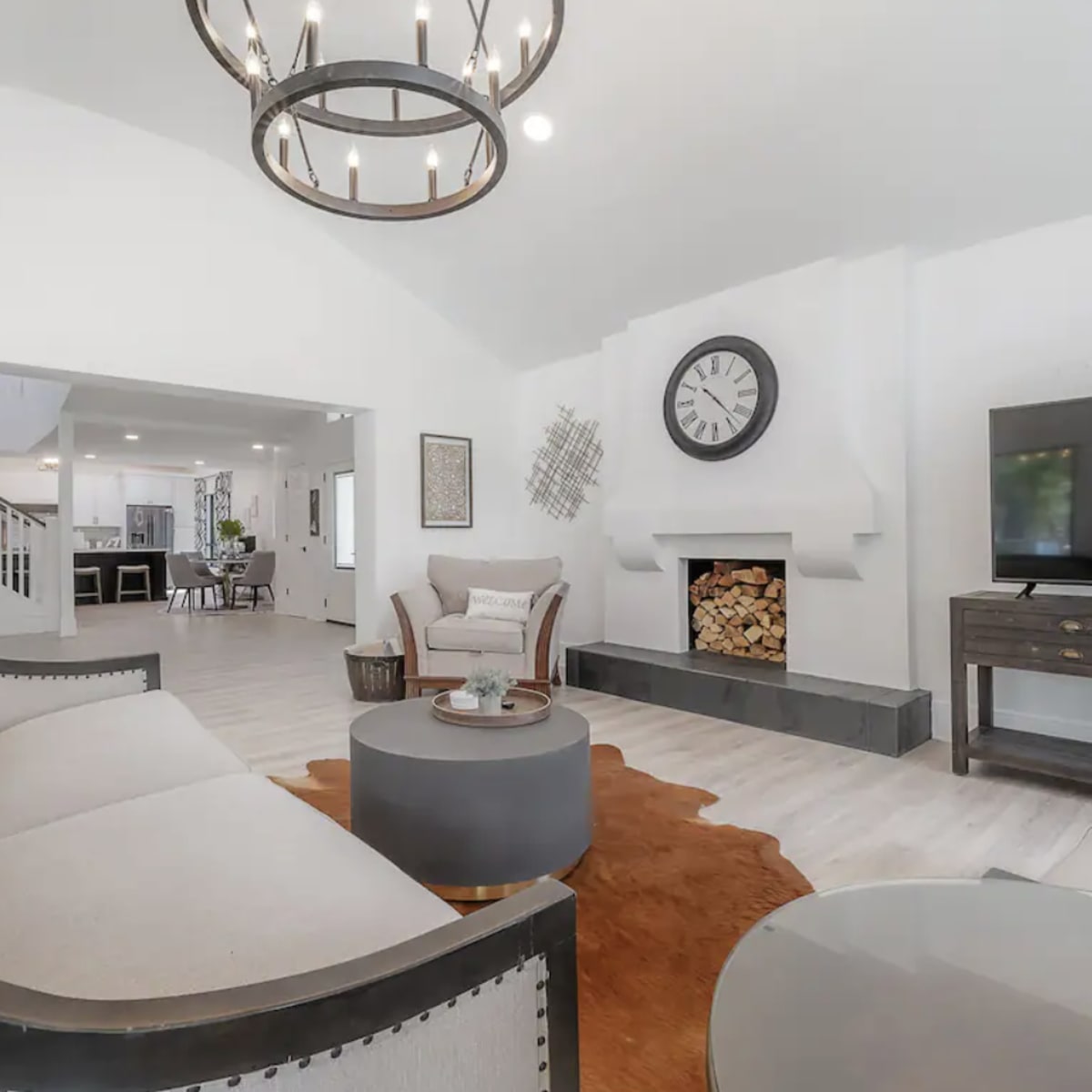 The room features a light-colored seating area with a fireplace, a wooden coffee table, and a visible open layout leading to another space.
