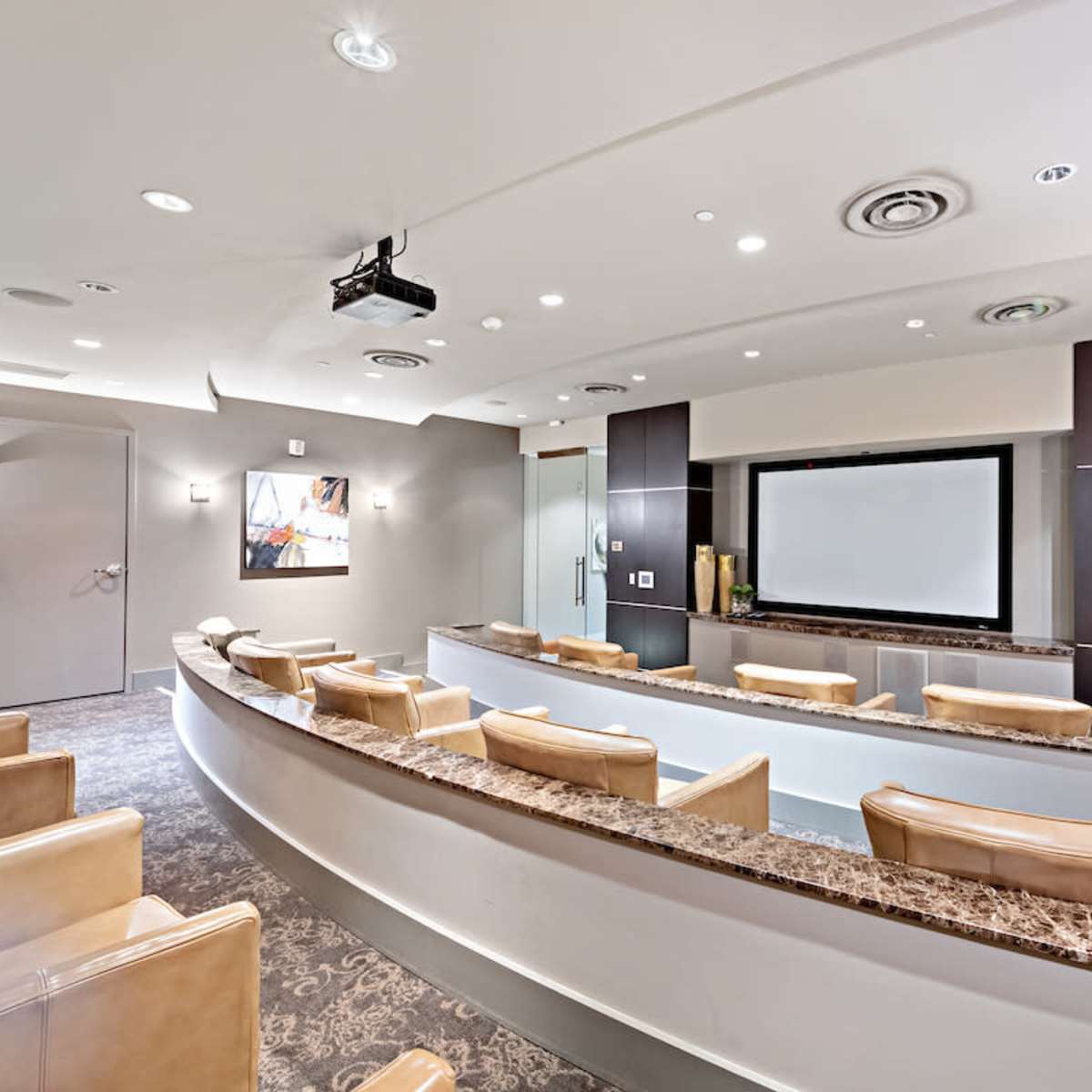 A modern conference room with tiered seating, a large screen at the front, and a projector installed in the ceiling.