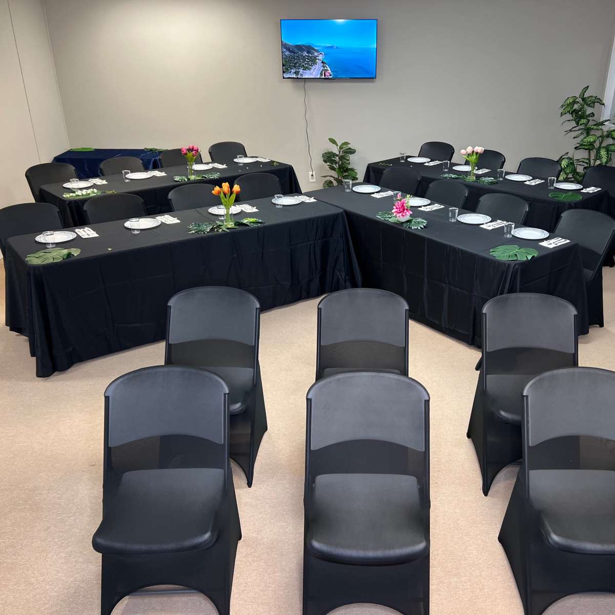 A meeting room is arranged with several tables covered in black cloth, set for a presentation, and black chairs facing the tables.